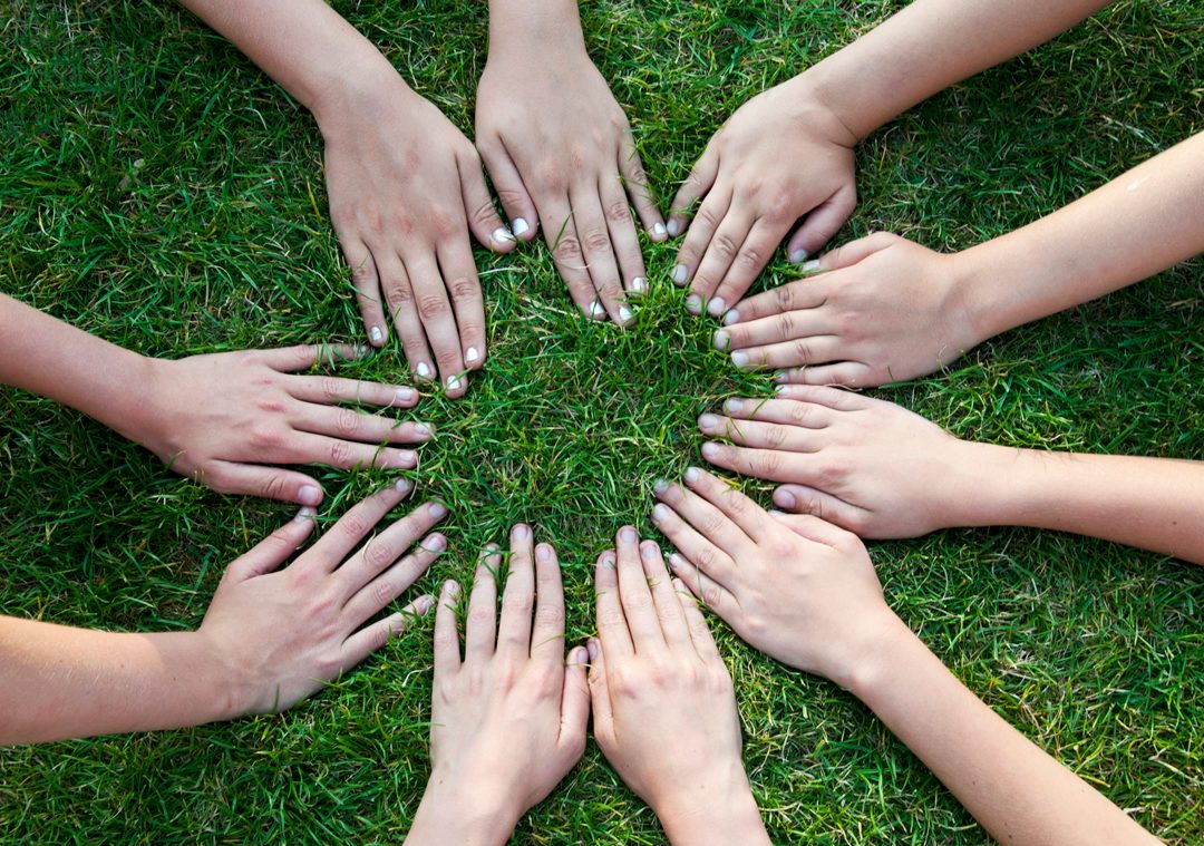 A circle of hands resting on green grass
